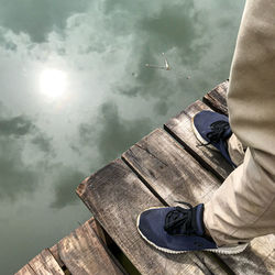 Low section of man standing by lake against sky