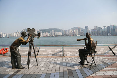 People photographing sea by cityscape against clear sky