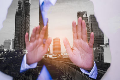Cropped image of hand holding modern buildings in city