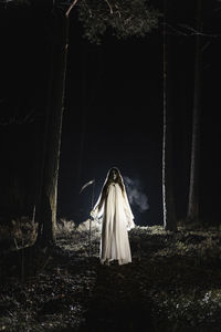 Ghost with scythe standing in forest at night
