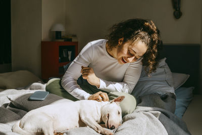 Young woman stroking dog lying on bed at home