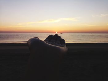 Scenic view of sea against sky during sunset, silhouette of a hand holding the rising sun 