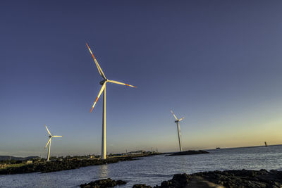 Windmills by sea against sky