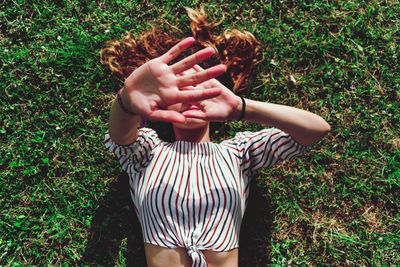 High angle view of woman covering face with hands while lying on field