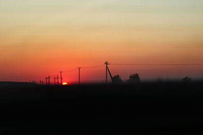 Silhouette electricity pylon on land against romantic sky at sunset