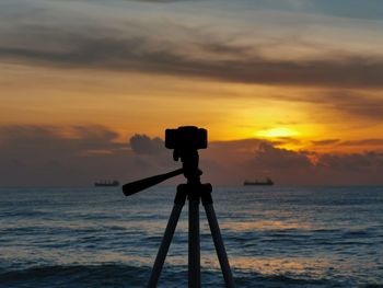 Silhouette camera on sea against sky during sunrise