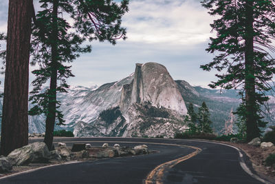 Road amidst trees and mountains against sky