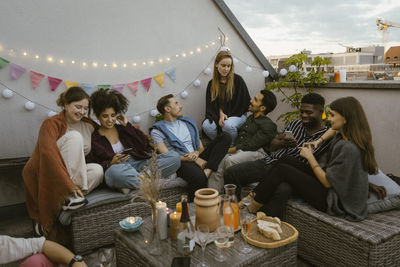 Group of male and female friends sitting and talking with each other at party in decorated balcony