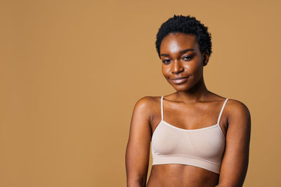 Portrait of young woman standing against yellow background