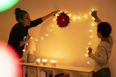 Smiling mother with son decorating illuminated christmas lights on wall at home
