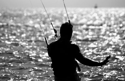 Rear view of silhouette man kiteboarding on sea