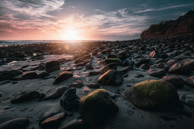 Rocks on beach against sky during sunset