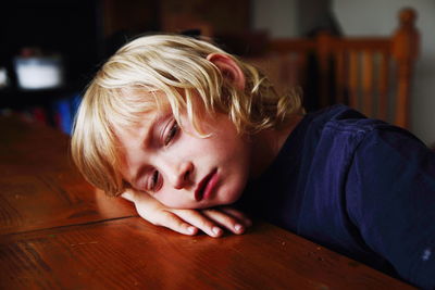 Bored blond boy resting head on table at home