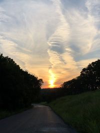 Road amidst trees against sky during sunset