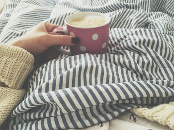 Cropped hand of woman holding coffee cup on bed