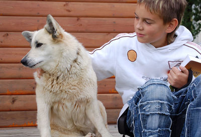 Cute boy sitting with dog against wall