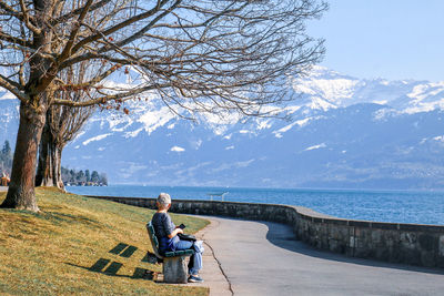 Man sitting on tree looking at sea against sky