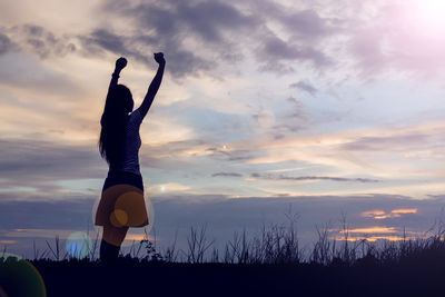 Silhouette woman with arms raised standing against sky during sunset