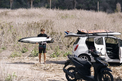 Young man with surfboard near car