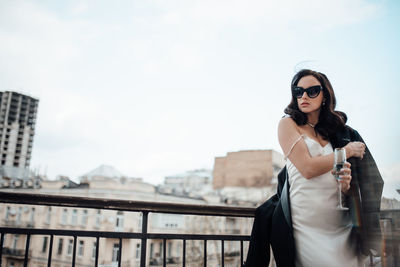 Young woman standing on railing against sky