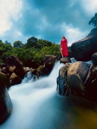 People on rocks by waterfall against sky