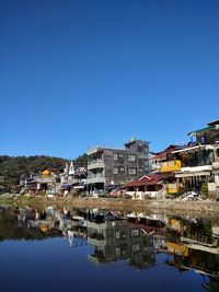 Reflection of buildings in lake against clear blue sky