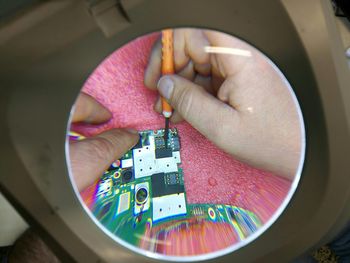 Cropped hands of male technician repairing chip seen through magnifying glass