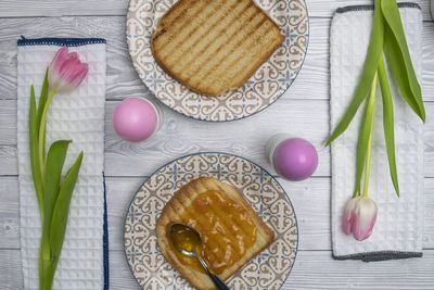 Colored easter egg in plate on a breakfast table with jam and pink white tulips.