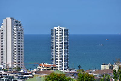 Sea by modern buildings against clear blue sky
