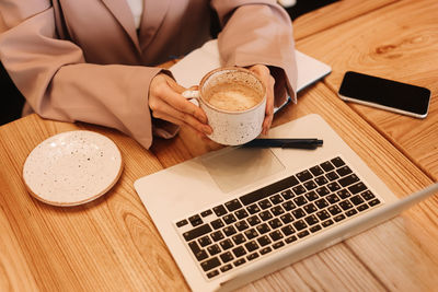 Human hands are typing on a laptop standing on a wooden table. desktop with a coffee mug