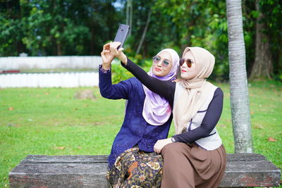 Young woman using mobile phone while sitting on tree