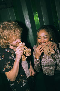 Young friends eating sandwich while enjoying at nightclub