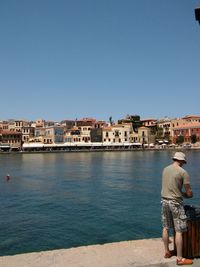 Rear view of people on river by buildings against clear sky