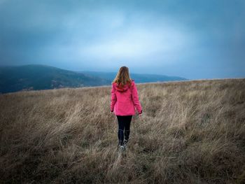 Rear view of woman with bright pink coat standing in the middle of a field on a cloudy day