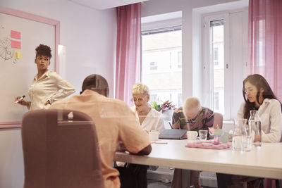 Coworkers having business meeting, woman writing on whiteboard