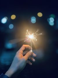 Cropped hand holding sparkler at night