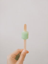 Close-up of hand holding ice cream against white background