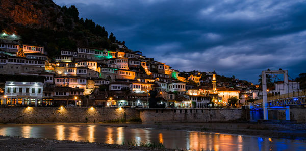 Illuminated buildings by river against sky at night