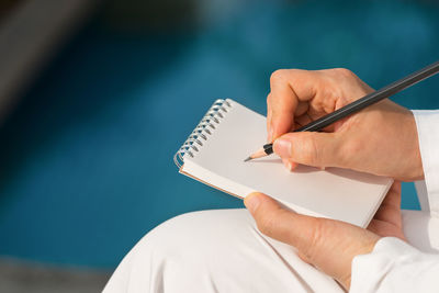Close-up of woman writing on notepad with pencil