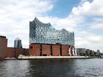 Modern buildings by river against sky in city