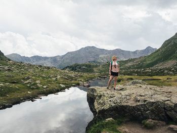 Mid adult woman standing on rock by lake against cloudy sky