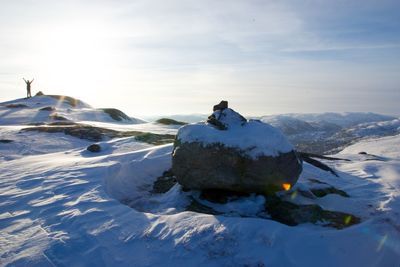 Woman with arms raised standing on snow covered mountain against sky