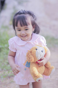 Cute girl holding teddy bear while standing outdoors