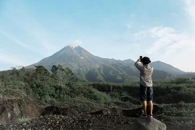 Rear view of man photographing mountains against sky