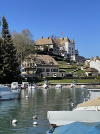 Sailboats moored in river by buildings against sky