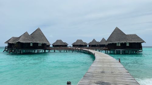 Stilt houses on pier by sea against sky