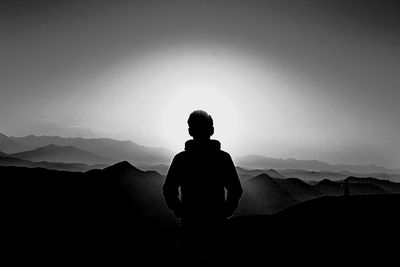 Rear view of silhouette man standing on mountain against sky