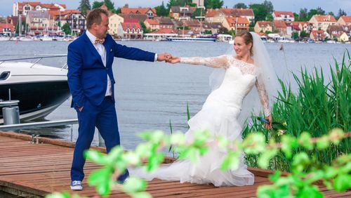 Wedding couple holding hands while standing on wooden jetty at mikolajki