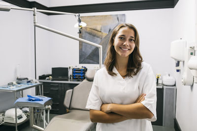 Smiling female dentist assistant standing with arms crossed in office