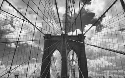 Low angle view of suspension bridge against cloudy sky